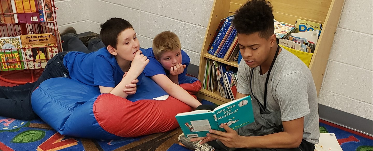 High School student reading with Elementary students